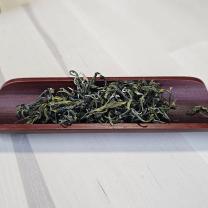Dried green tea leaves in a wooden holder on a white wooden surface
